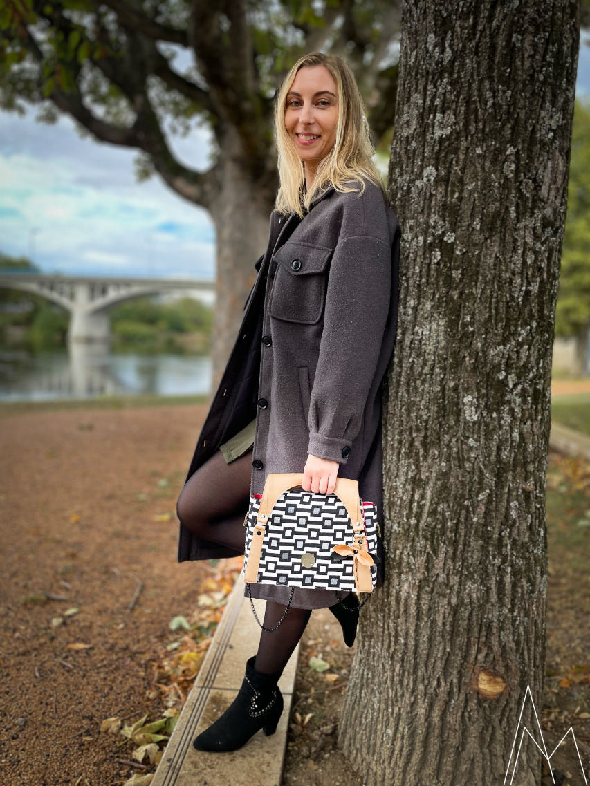 Photo d'une jeune femme blanche et blonde portant un sac d'épaule noir et blanc et caramel, dans un parc en extérieur, de jour.